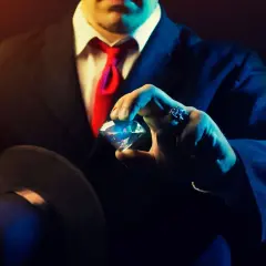 Mężczyzna w garniturze i czerwonym krawacie trzyma brylant, jakby grał w mafijną grę o najwyższą stawkę.