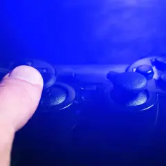 Dłoń naciska joystick kontrolera do gier w niebieskim świetle.