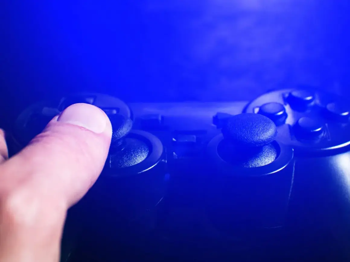 Dłoń naciska joystick kontrolera do gier w niebieskim świetle.