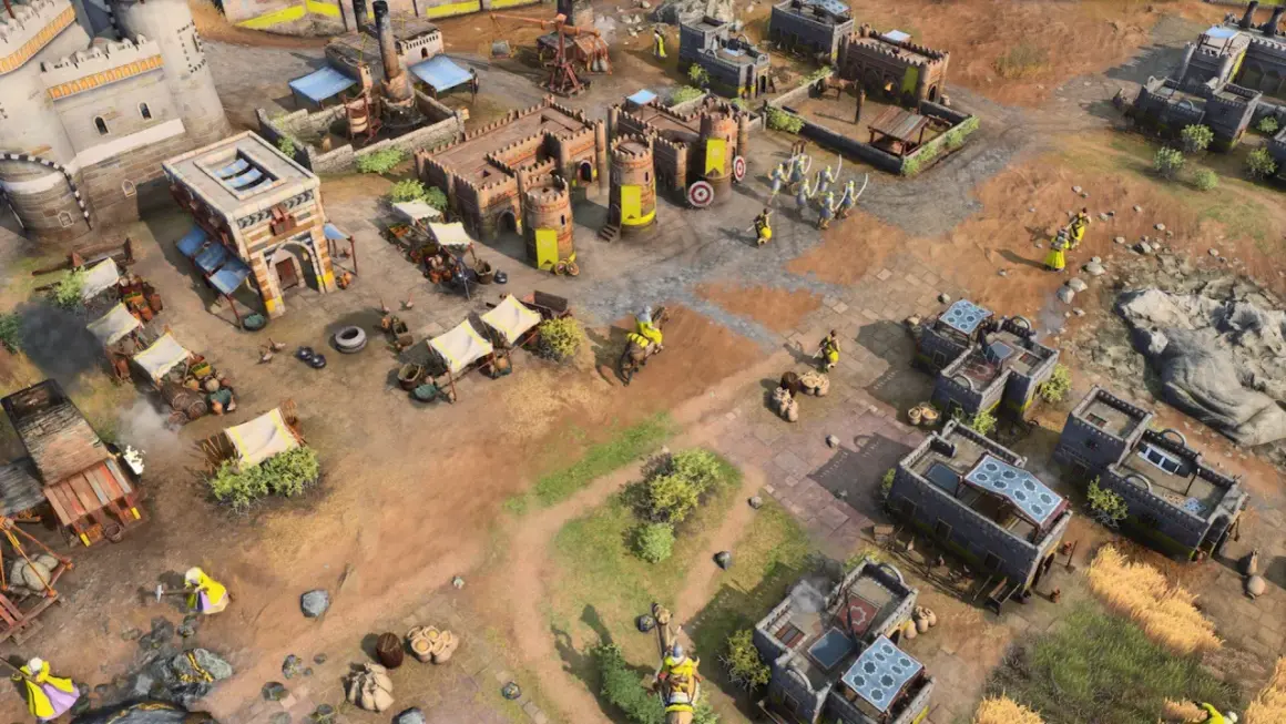 Scena z gry rts: zamek, budynki, rycerze w żółtych strojach, wozy i targowisko.