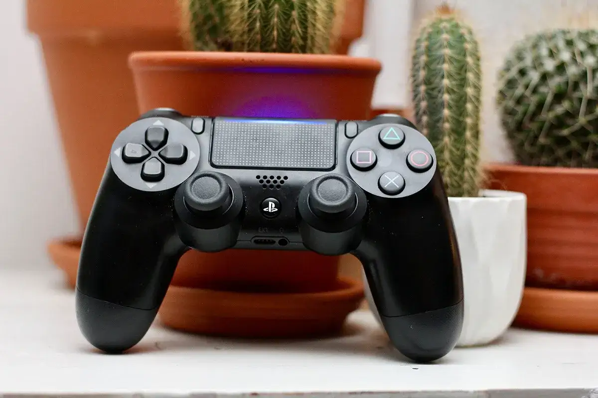 Czarny pad DualShock 4, gotowy do gry. W tle kaktusy w doniczkach.