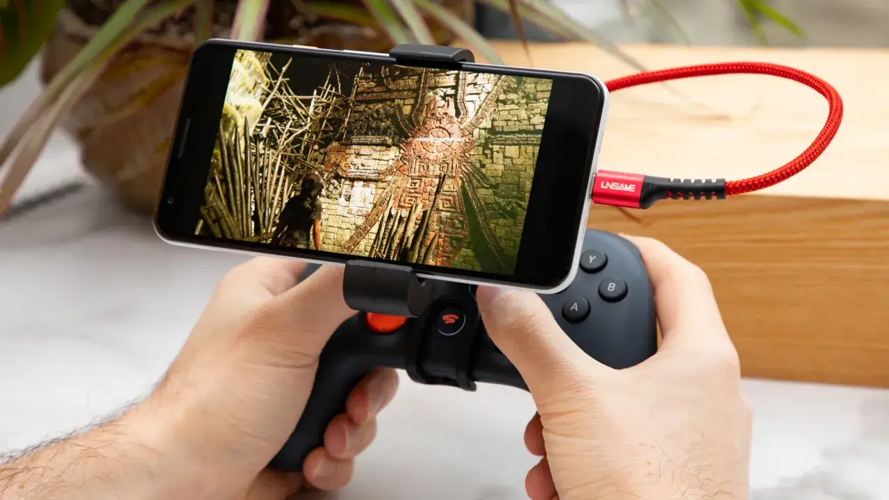 Ręce trzymają smartfon z grą przygodową, podłączony kablem do kontrolera. To idealne rozwiązanie do grania w gry na stadia.