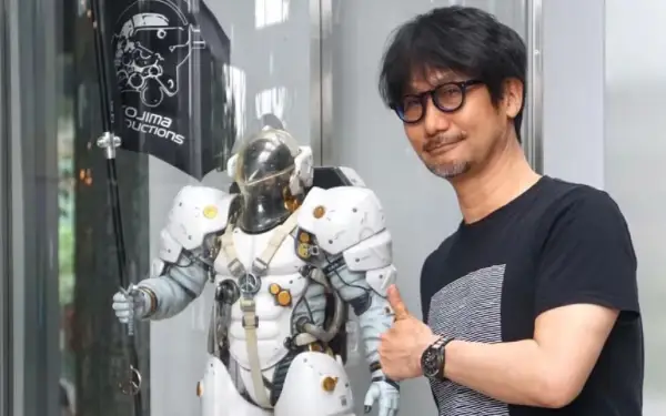 Hideo Kojima z kciukiem w górę obok postaci z gry, z logo Kojima Productions w tle.