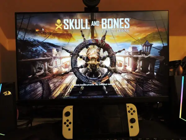 Logo gry "Skull and Bones" z kołem sterowym ozdobionym czaszką i kośćmi.