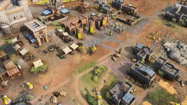 Scena z gry rts: zamek, budynki, rycerze w żółtych strojach, wozy i targowisko.